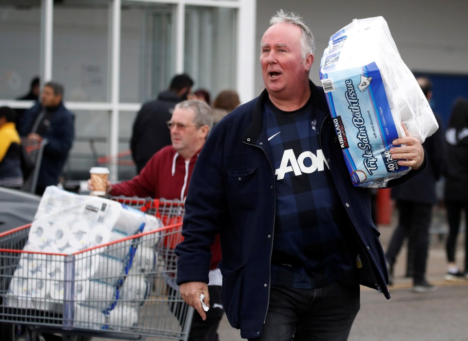  Customers carry toilet roll as they leave a Costco in Manchester