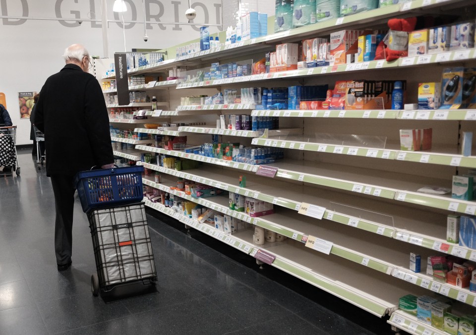 A man with a shopping trolley walking past empty shelves in a Sainsbury’s store in London