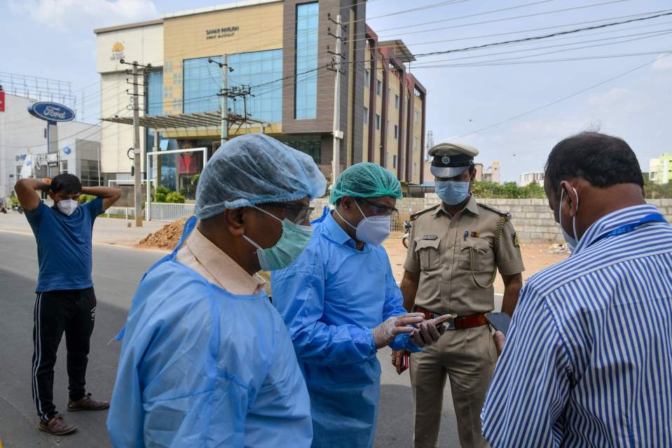 Paramedics, government municipal and police officials stand outside a private hotel as they plan the safe evacuation and hospitalisation of a suspected positive COVID-19 coronavirus customer that allegedly self-quarantined himself in the hotel in Bangalore