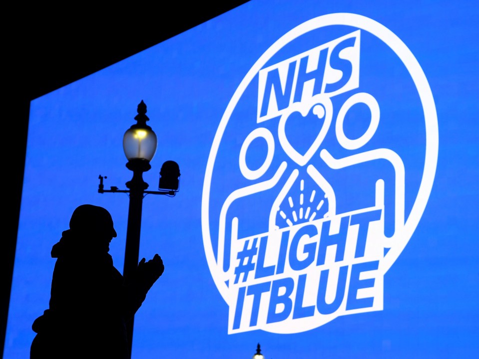  A person claps in front of a NHS sign in Piccadilly Circus