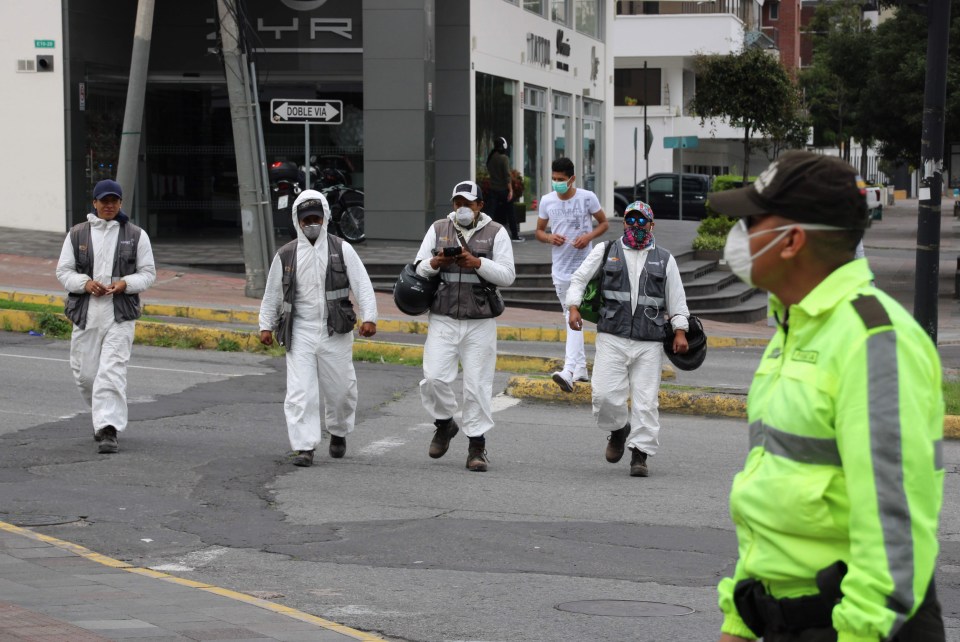  Telecom workers in face masks walk down a street in Quito, Ecuador