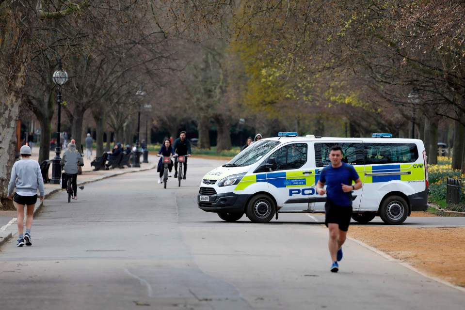  A police van drives past people taking their daily exercise allowance in Hyde Park, London