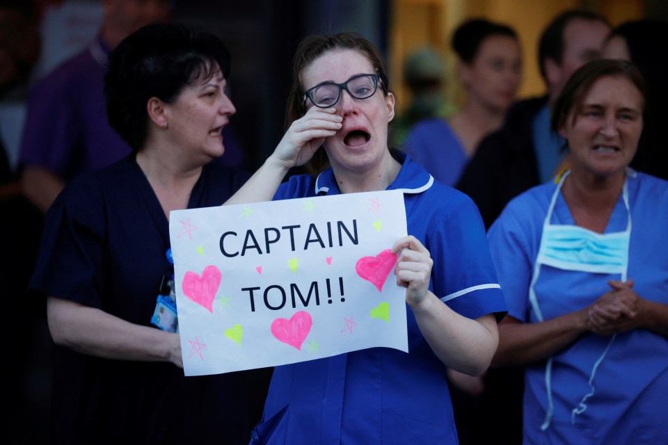 A crying NHS worker holds a message for WWII vet Captain Tom outside the Aintree University Hospital