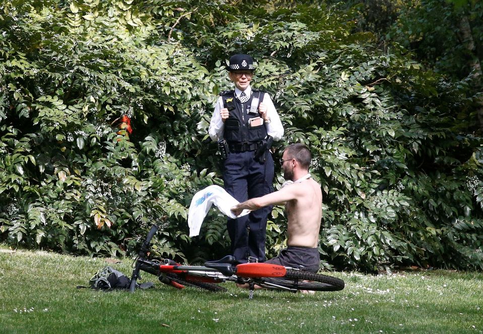  A police officer speaks with a sunbather in St James' Park in London