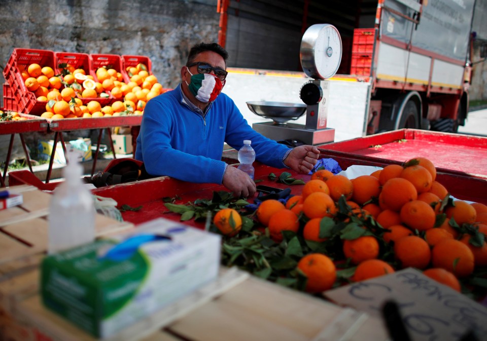  A fruit seller wearing a face mask sits at his stall in Cisternino, Italy