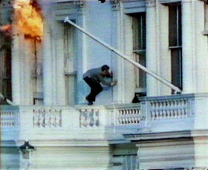  Fire rages from the window of the embassy as hostage Sim Harris escapes from a window