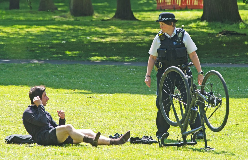  A police officer on patrol asks a cyclist to stop sunbathing and move on in Greenwich, London