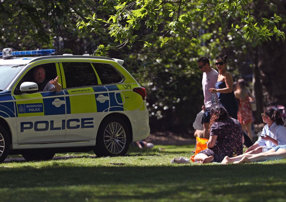 Police officers in a patrol car move sunbathers on in Greenwich Park, London