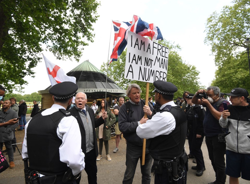  An anti-lockdown protester holding a banner reading 'I am a free man, I am not a number' argues with police officers