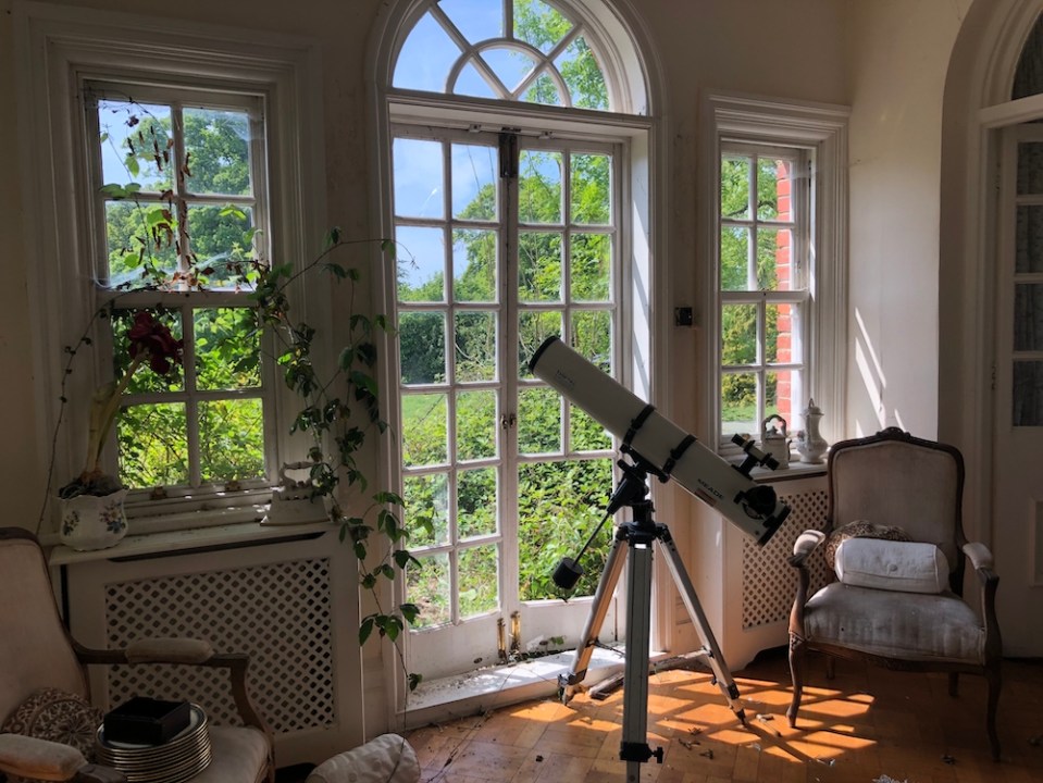  A telescope stands ready for use, but the house has been left for so long that a vine has started to grow through a window