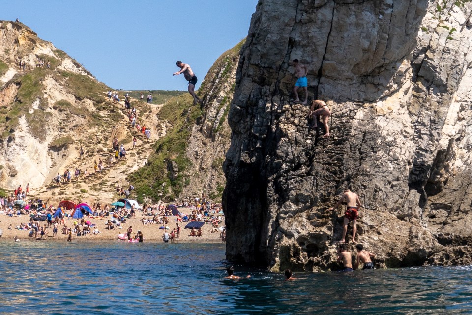 People jump from a lower part of the rocky arch