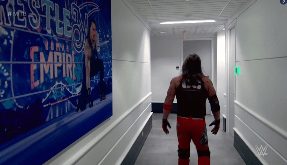  Roman Reigns can be seen on the wall with AJ Styles appearing in the MITB match