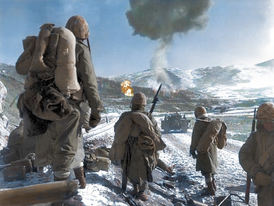 American troops look on as explosions break up the snowy terrain during the Korean War