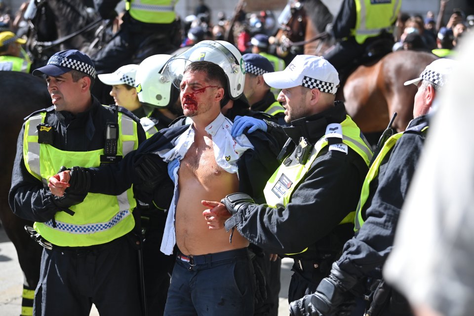 A bloodied member of the group is led away by police