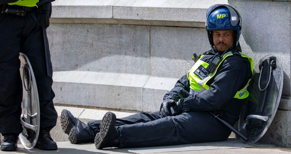 An exhausted officer in riot gear slumps on the pavement