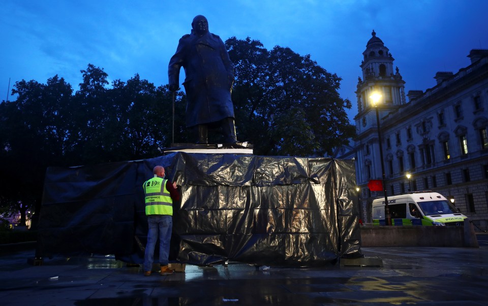 A worker stands near the base of the Winston Churchill statue covered in a black tarp lat night