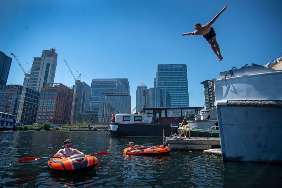  A swimmer dives into the water at the London Docklands in front of the skyline of Canary Wharf