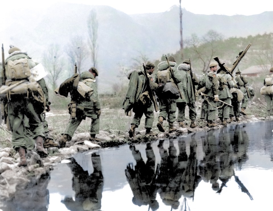 US soldiers trudge along the edge of a bank 