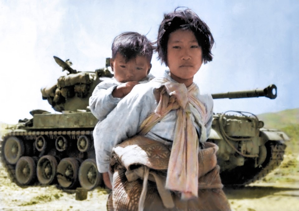 With her brother on her back, a war-weary Korean girl trudges by a stalled M-26 tank in Haengju