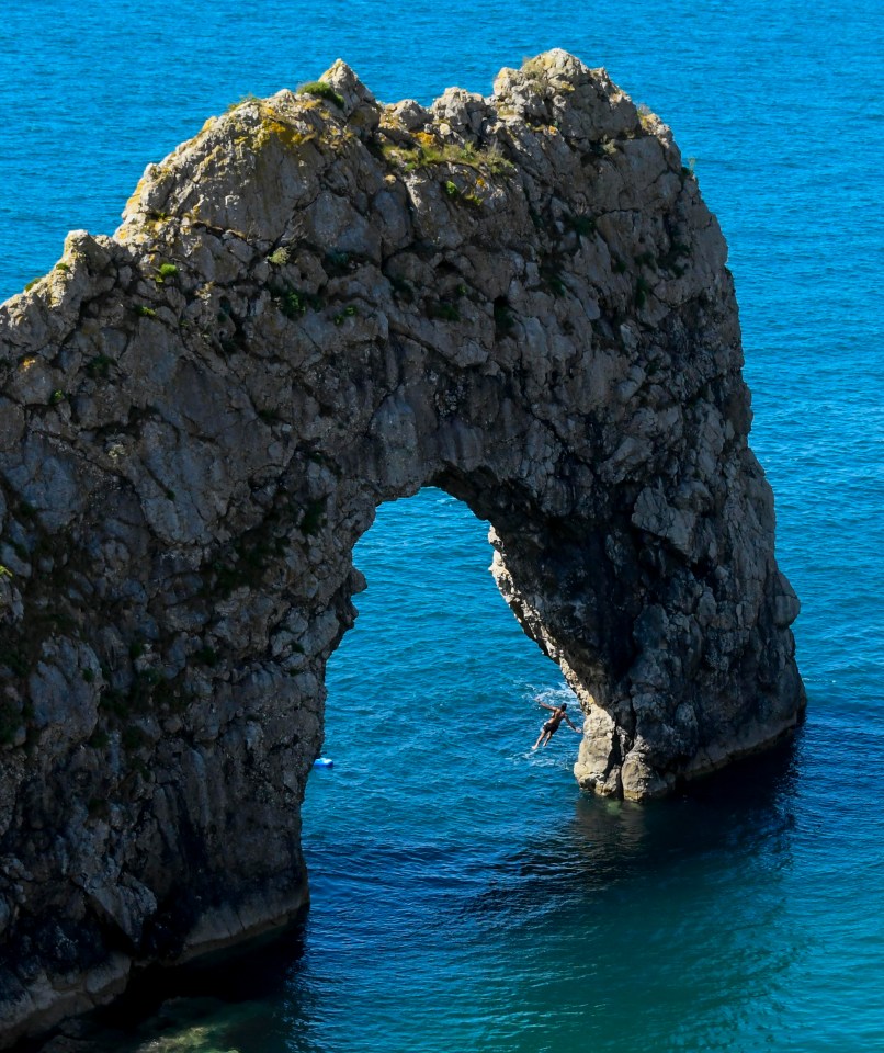 A thrillseeker jumps from the top of the Durdle Door rock arch in Dorset