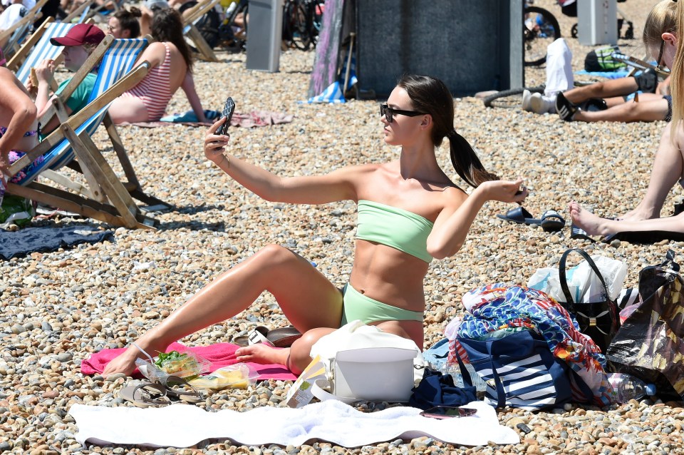 A sunbather takes a selfie at a busy Brighton beach