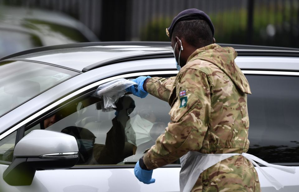 A member of the military passes a testing kit through a car window