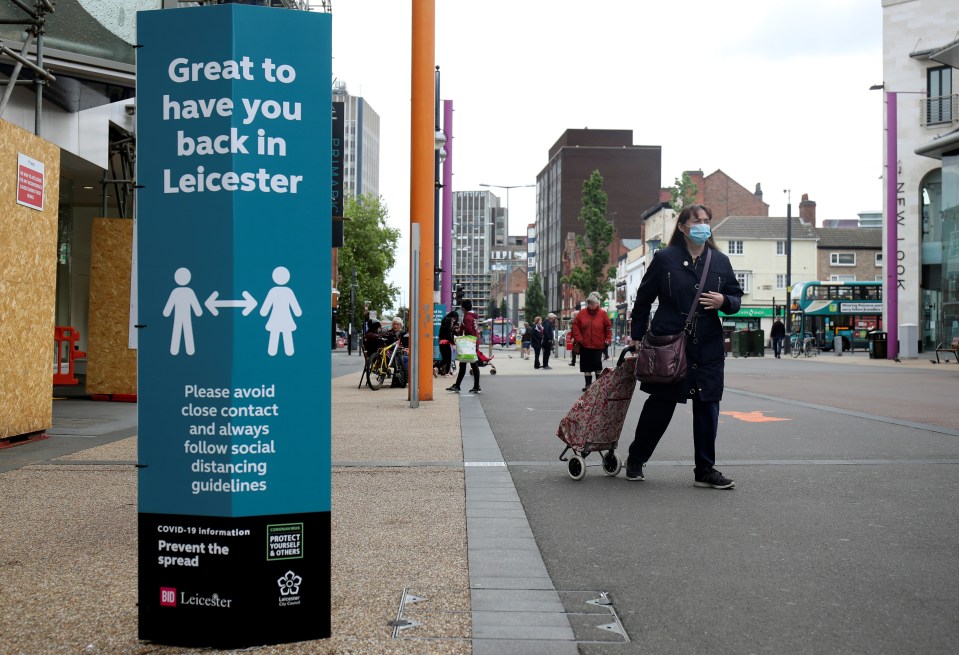 A woman wearing a mask walks past a sign which reads 'Good to have you back in Leicester'