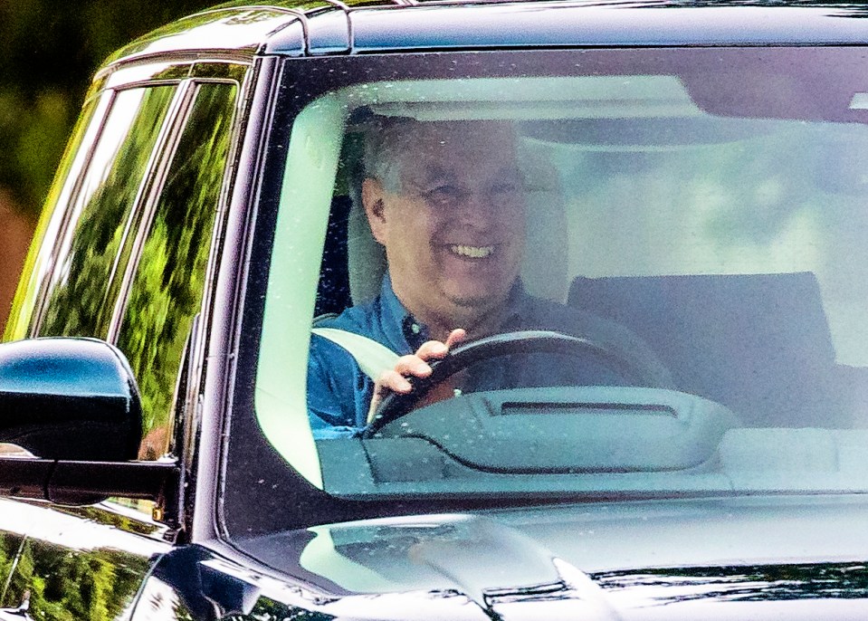 A smiling Prince Andrew behind the wheel in his Range Rover as he leaves his Royal Lodge home on July 15