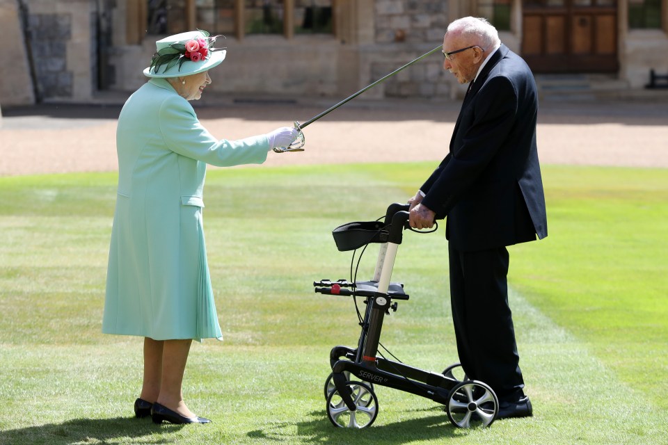 The pair grin as the Queen knights Captain Sir Tom at Windsor Castle