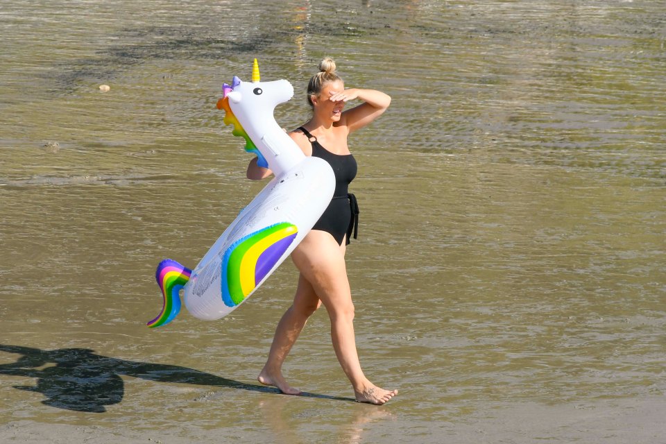 A woman with a unicorn rubber ring takes a stroll across the sands at Lyme Regis