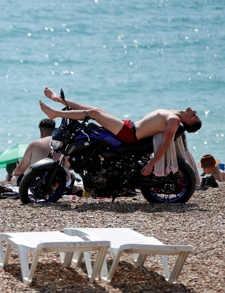 A man sunbathes on top of a motorbike on Brighton beach