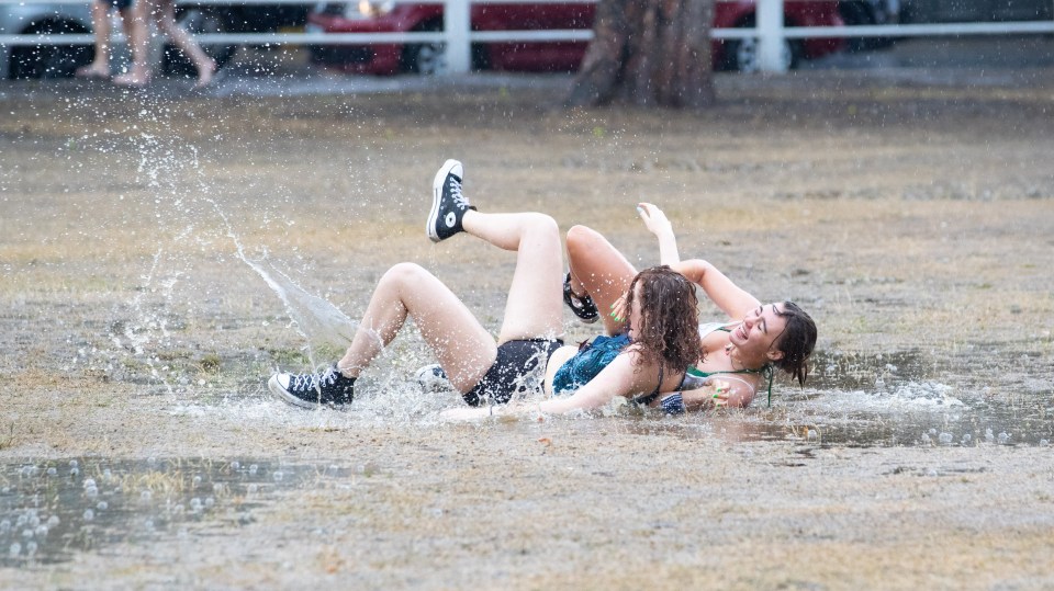 Two friends have fun in the puddles created after torrential rain and hail on Twickenham Green