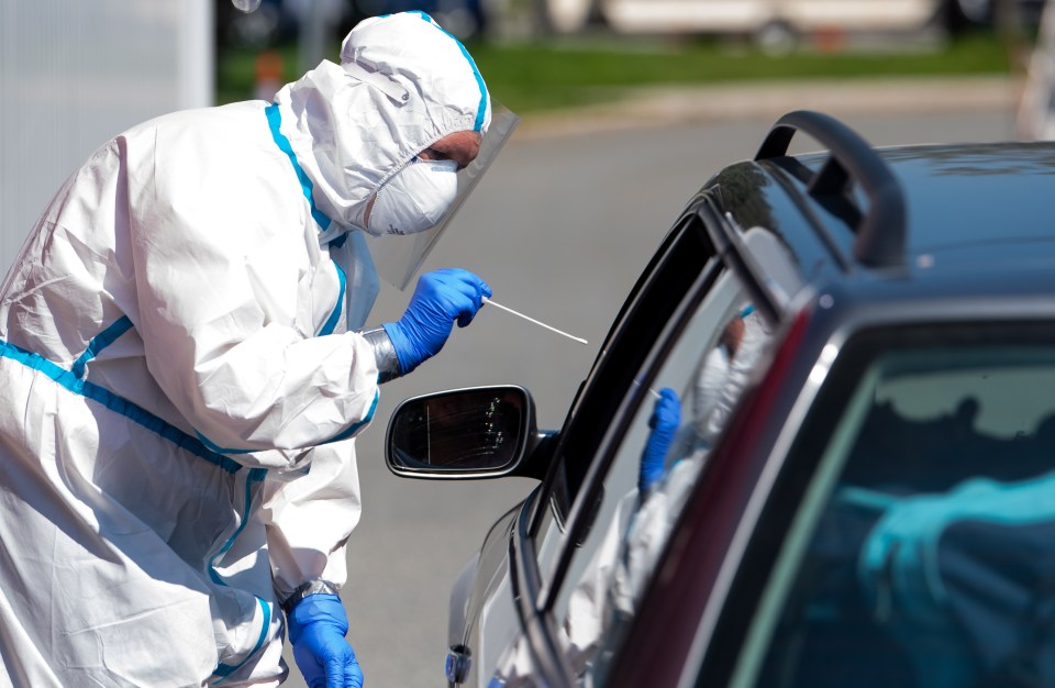 An employee of the Bavarian Red Cross takes a smear test on a car driver at a corona test centre as the local government launches a test offensive