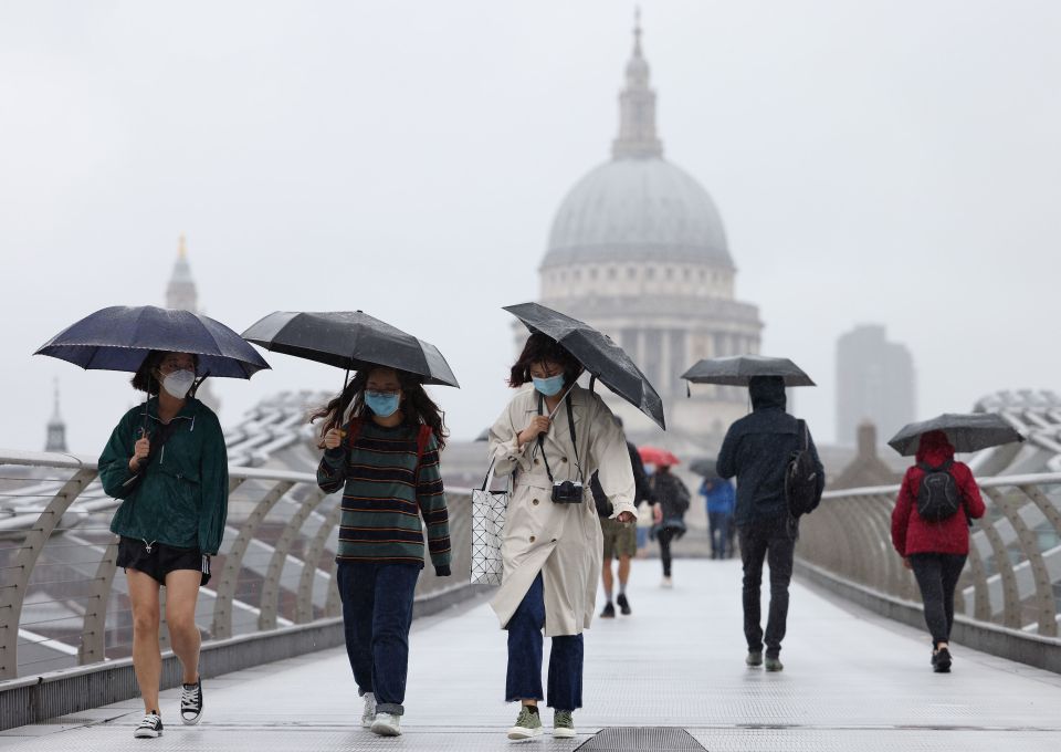 People caught in heavy rain with gusty winds while walking along the Millennium Bridge in London