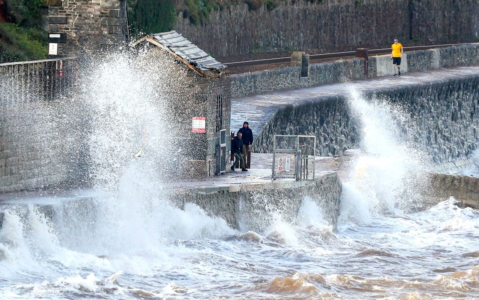 People walk past waves in Dawlish, Devon as gusts of up to 60mph could hit coastal areas