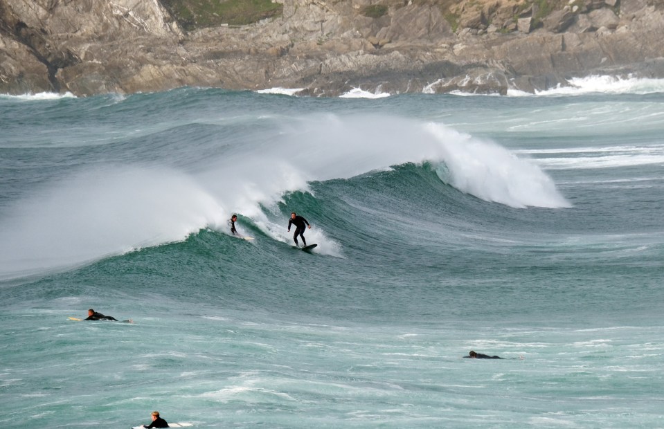 Surfers riding waves as Storm Ellen starts to roll in on Fistral Beach, Cornwall