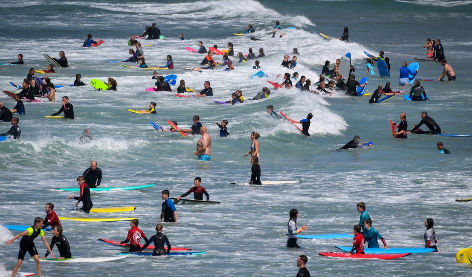 Tourists enjoy bodyboarding and surfing at the beach at Polzeath on July 30 