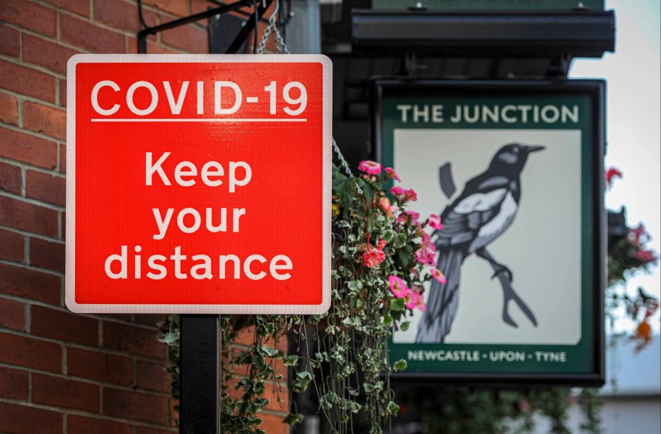 Covid warning signs next to a pub sign in Newcastle city centre urging people to maintain social distancing