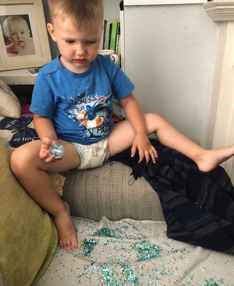 The tot looks perplexed after dropping a pot of sequins on the sofa