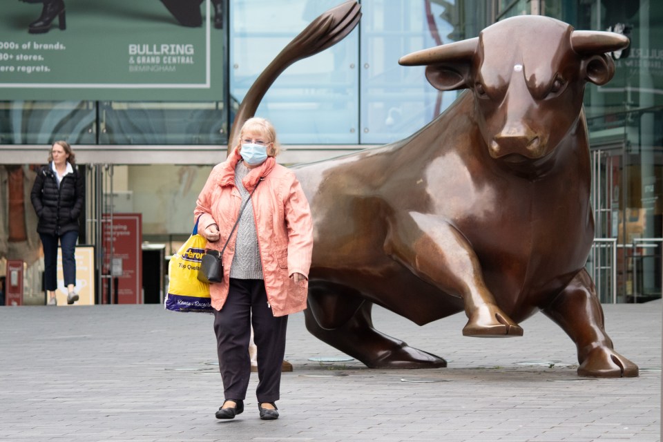 A woman wearing a mask walks past the Bull Ring shopping centre in Birmingham