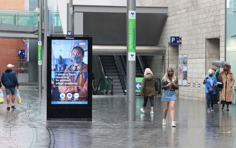 Shoppers walk past a sign urging people to wear masks 