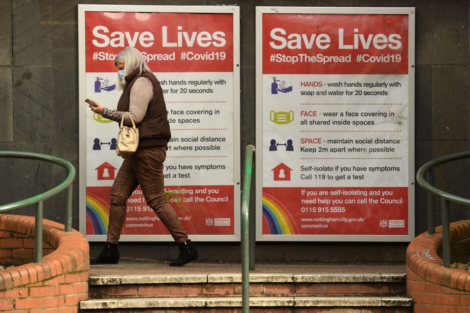 A woman wearing a mask walking past a Covid warning sign in Nottingham