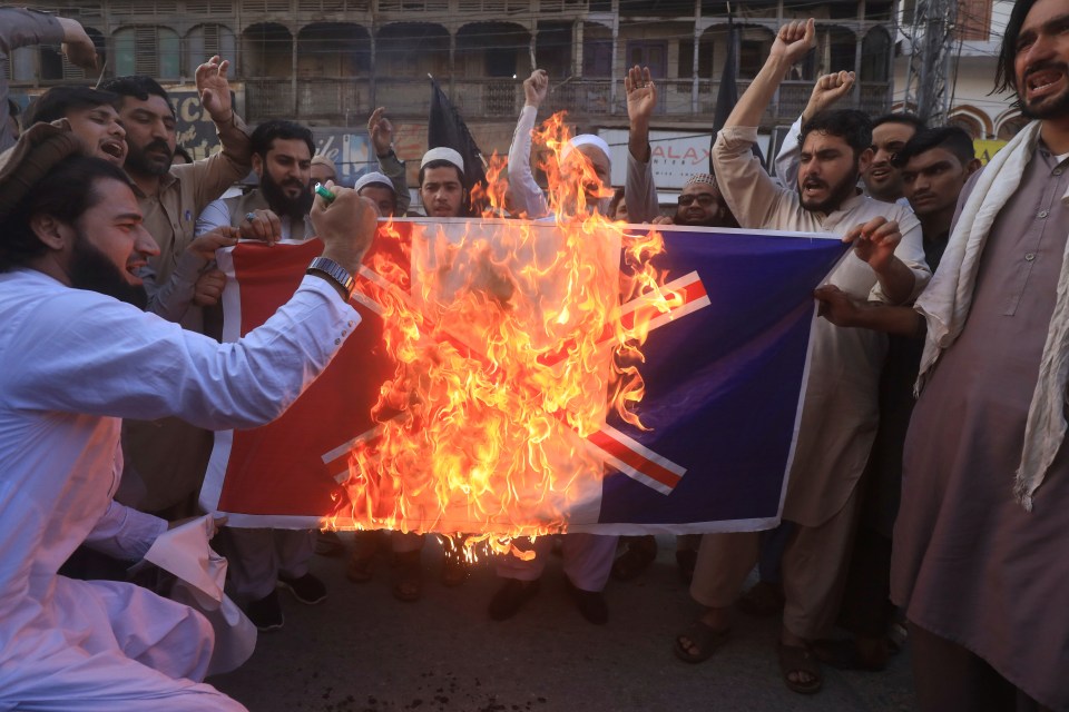 People chant slogans as they set fire to a banner with a crossed-out France's flag during a protest in Pakistan 