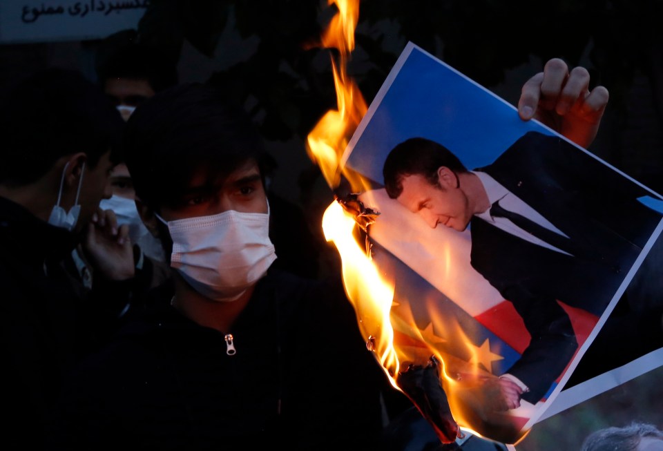 A protester in Iran burns an image of Emmanuel Macron