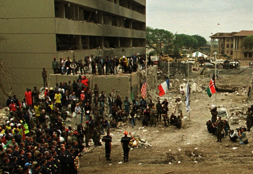 The flags of the United States, France, Israel and Kenya fly half staff amid the ruins