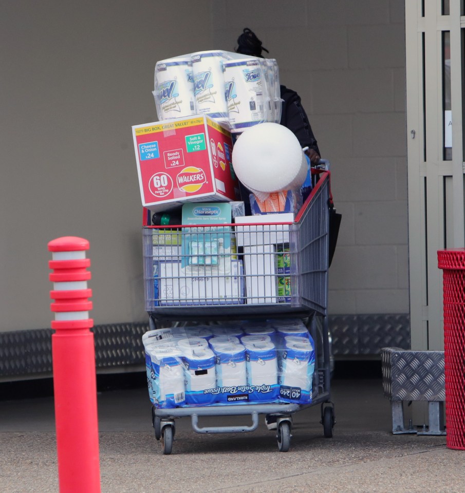 A woman wheels a trolley full of essentials out the store