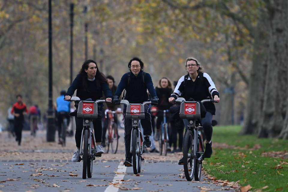 Three women are seen cycling at a busy Green Park in London