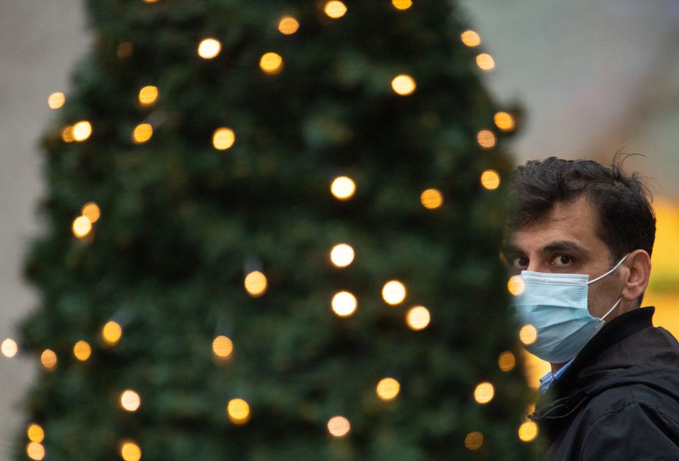 A man wearing a face mask passes Christmas lights outside a shop in central London