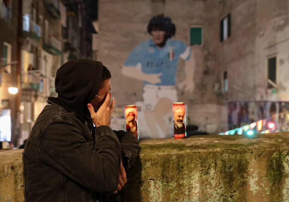 A man wipes away tears in front of a giant mural of Maradona