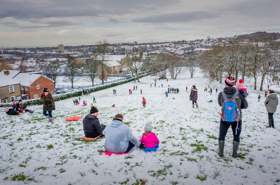 A family prepare to sledge down a hill as people enjoy the snow in Cheetham Park in Stalybridge